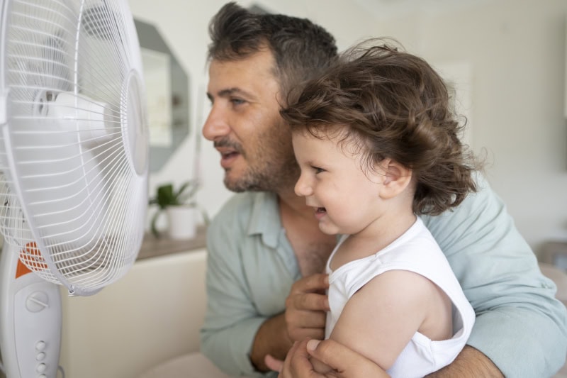 father and toddler in front of a fan.