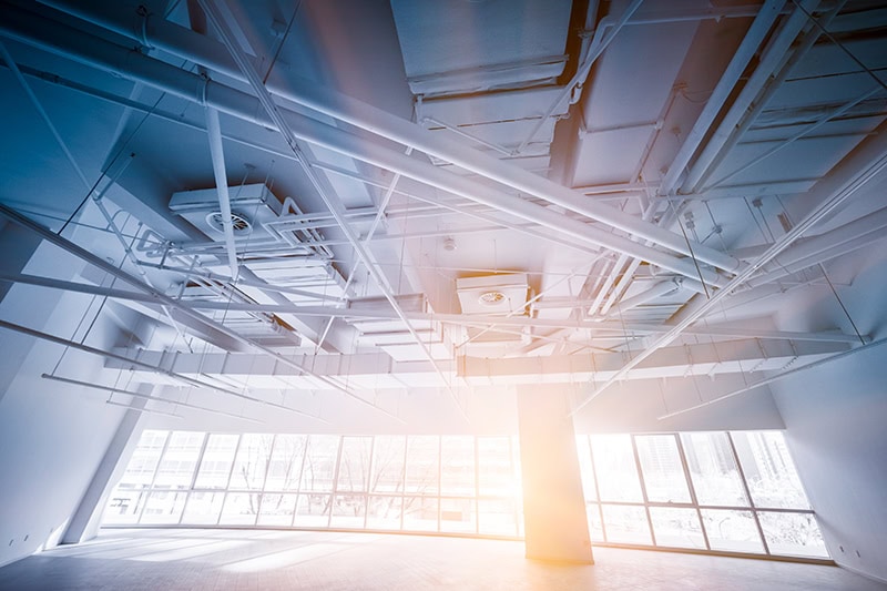 The exposed ceiling infrastructure of a large, empty commercial space or office building is shown from a low angle.