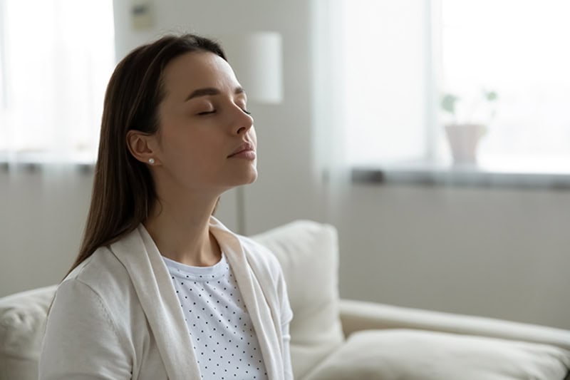 A women taking a deep breath with her eyes closed.