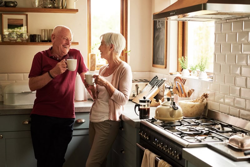 What Size Heat Pump Do I Need? Photo of an elderly couple sipping a hot beverage together in their kitchen.